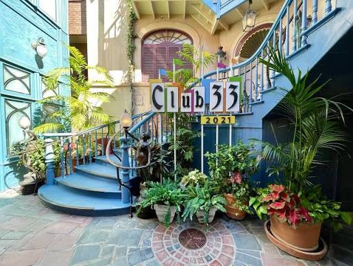 Court of Angels atmosphere near Club 33 with blue railings, warm lamp light, and a bronze figure.